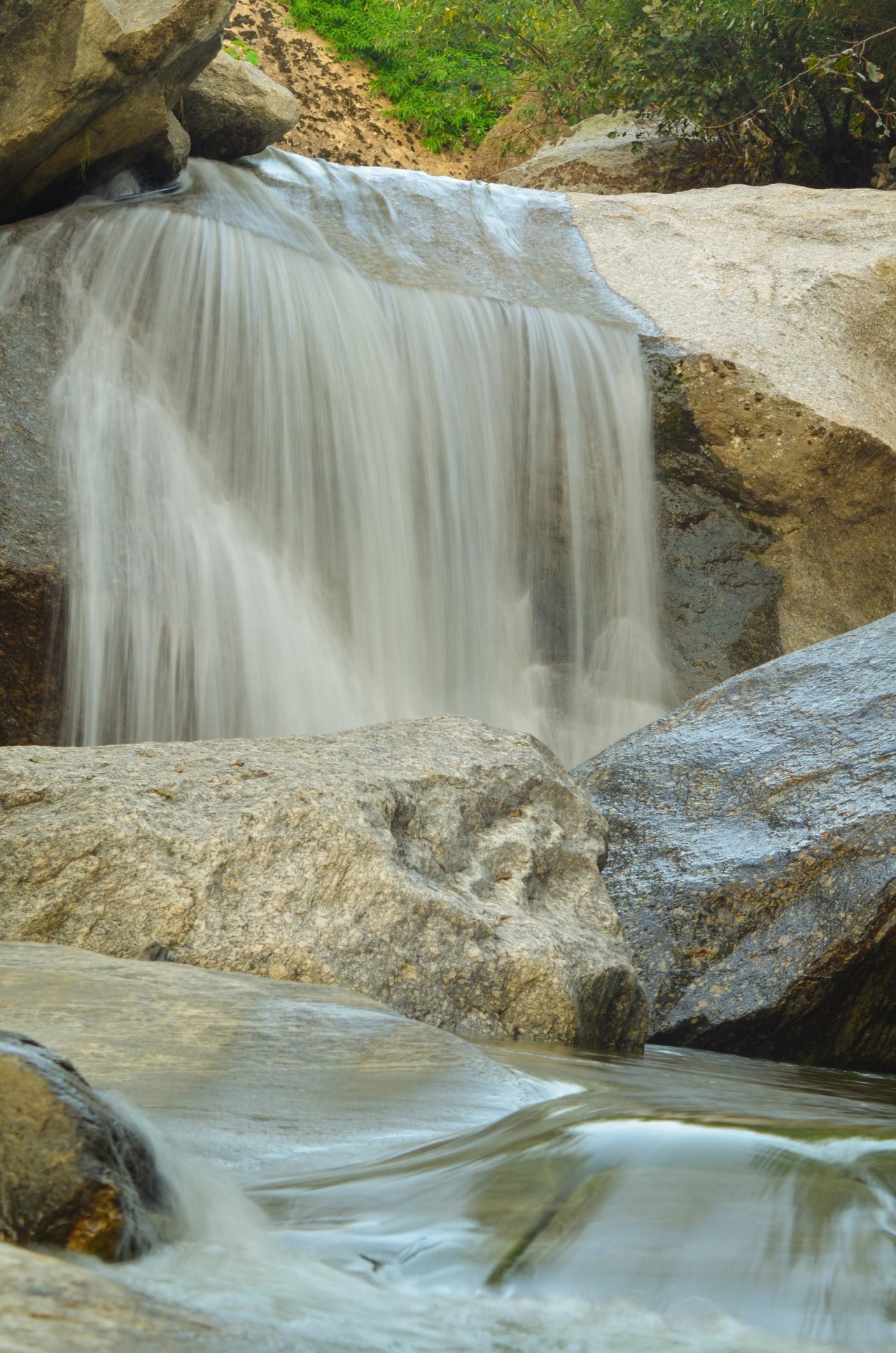 Serene waterfall flowing over smooth rocks, surrounded by lush greenery and natural beauty. Free Landscapes photos